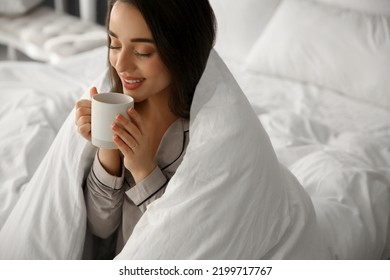 Beautiful Young Woman Wrapped With Soft Blanket Holding Cup Of Hot Drink On Bed At Home