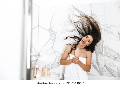 Beautiful young woman wrapped in a towel standing over marble background, holding hair brush, singing - Powered by Shutterstock