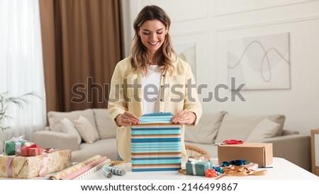Beautiful young woman wrapping gift at table in living room