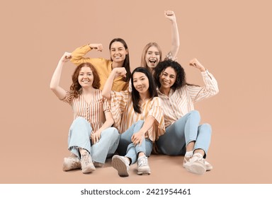 Beautiful young women with clenched fists sitting on beige background. Women history month