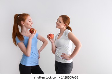 Beautiful young women eating fresh apples on light background