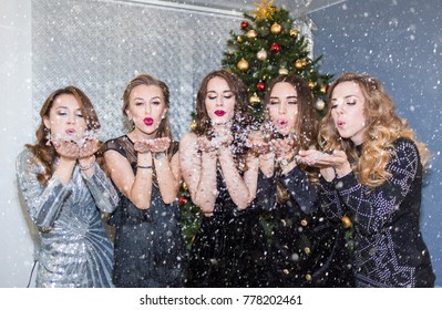 beautiful young women having fun at a Christmas party, blowing away confetti and snow, sending kisses. - Powered by Shutterstock