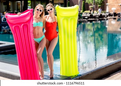 beautiful young women with inflatable mattresses standing at poolside and looking at camera