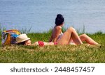 Beautiful young women sunbathe in summer on a grassy beach by the lake next to a beach chair