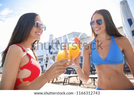 Beautiful young women in swimming suits drinking cocktails at resort on summer day