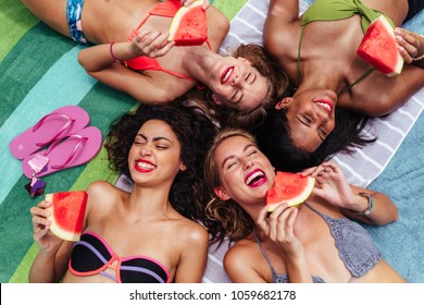 Beautiful young women in swimsuits lying on towel and eating watermelon by the poolside. Group of female friends hanging out by a resort swimming pool. - Powered by Shutterstock