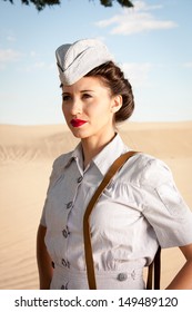 A beautiful young WWII nurse, in authentic uniform, stares off into the dry dusty landscape. close up head and shoulders.