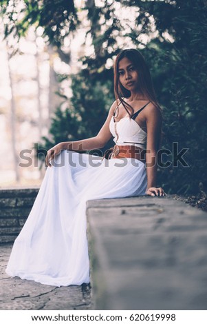 Beautifull girl in long white dress sitting, posing in the park 