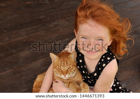 beautifull smiling red hair little girl sitting and holding a ginger cat. red hair model.  ginger girl. cute and pretty small girl in dress.