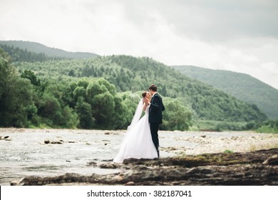 Beautifull wedding couple kissing and embracing near the shore of a mountain river with stones 