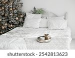 A beautifully arranged bedroom features a cozy bed with white linens and pillows. A decorated Christmas tree nearby adds a touch of holiday cheer, enhancing the festive atmosphere.