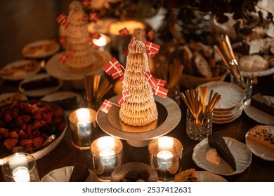 A beautifully arranged dessert table featuring pastries, danish cheeses, cakes, and a large floral centerpiece with red roses and hydrangeas. Soft candlelight creates a warm, inviting ambiance - Powered by Shutterstock