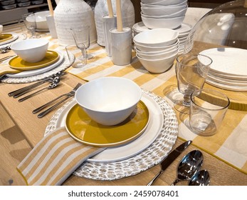 A beautifully arranged dining table featuring modern tableware with a striking color palette of white and gold plates, complemented by striped napkins and clear glassware, set on a wooden table for a - Powered by Shutterstock