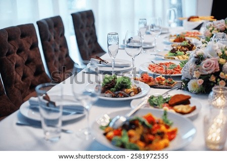 Beautifully arranged dining table featuring diverse culinary dishes, fine glassware, floral decorations, creating inviting and elegant atmosphere for dining events, gatherings, or formal celebrations.