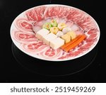 A beautifully arranged plate of thinly sliced raw meat, tofu, vegetables, and fish cakes, ready for hotpot or shabu-shabu cooking.