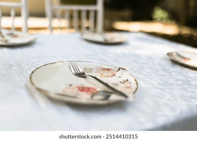 A beautifully arranged table features floral-decorated plates and silverware on a white tablecloth, illuminated by gentle afternoon sunlight. - Powered by Shutterstock