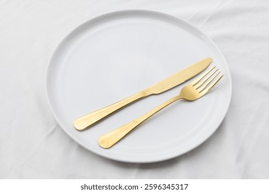 A beautifully arranged table setting displaying an empty ceramic plate, fork, and knife on a white tablecloth, evoking a clean and modern dining aesthetic.


