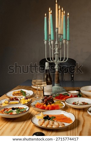 A beautifully arranged table showcases an array of colorful dishes, fruits, and a bottle of wine. Candles illuminate the setting, enhancing the warm, inviting atmosphere