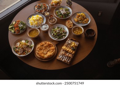 A beautifully arranged wooden table overflowing with a variety of delicious Mediterranean dishes. The spread includes hearty khachapuri, fresh salads, savory soups, crispy baked potatoes, rich sauces, - Powered by Shutterstock