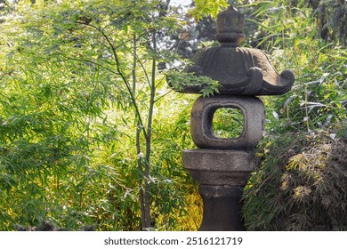 A beautifully crafted stone lantern surrounded by vibrant green foliage creates a tranquil atmosphere in a garden. Sunlight filters through the leaves, enhancing the peaceful setting. - Powered by Shutterstock