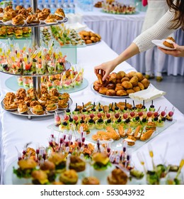 Beautifully decorated catering banquet table with burgers, profiteroles, salads and cold snacks. Variety of tasty delicious snacks on the table
