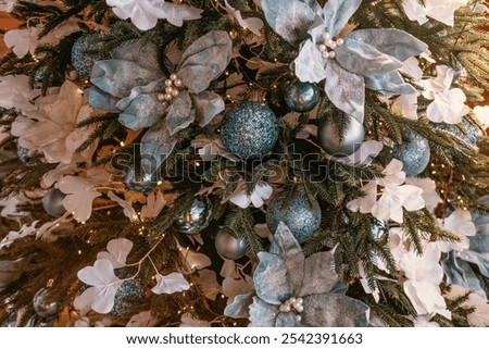 A beautifully decorated Christmas tree features blue and silver ornaments, complemented by white floral accents. The warm lights enhance the festive atmosphere in the room.