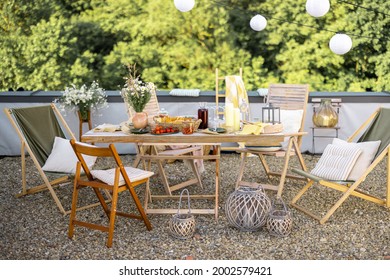 Beautifully Decorated Roof Terrace In Natural Boho Style With A Dining Table Full Of Food At Summer Time. Festive Dinner For A Small Group Of Friends Outdoors