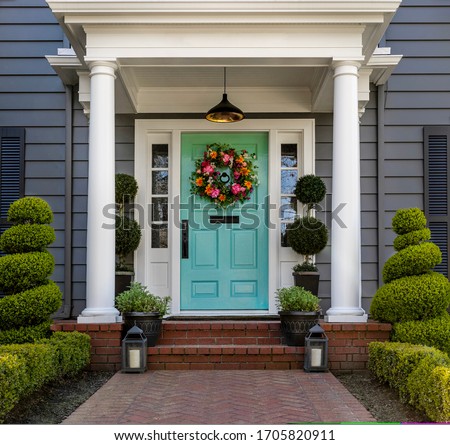 Beautifully decorated turquoise colored front door of traditional home. Brick path and trimmed hedges.