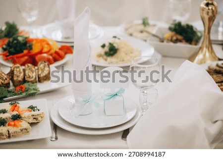 Beautifully decorated white table set for a celebration, featuring a folded napkin with ribbon and a small guest favor