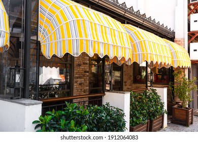 a beautifully designed vintage-style cafe, restaurant with colorful striped awnings, wooden flower beds with green plants and fancy wrought-iron lamps in Kemer, Turkey