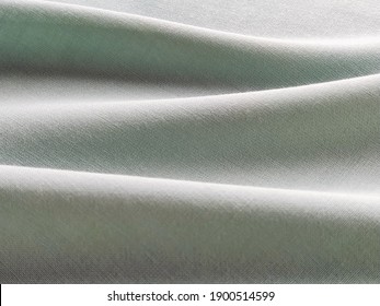 Beautifully Folded Light Green Fabric. Soft Pleasant Waves And Flounces On Textiles. Close-up. Drapery For Curtains, Fabric For Dressmaking Or Upholstery.