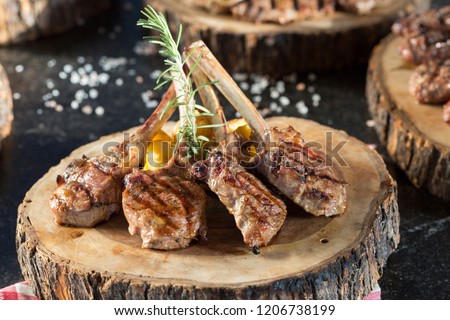 Beautifully grilled lamb rib chop steaks, medium rare with fried potato chips on wood serving board.