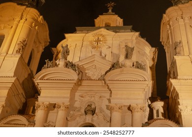 The beautifully illuminated church facade is a stunning display of intricate baroque architecture, adorned with exquisite sculptures, standing out magnificently against the night sky - Powered by Shutterstock