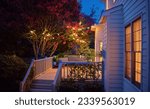 beautifully lit exterior of traditional house with wooden terrace and blooming crape myrtle in summer garden at night