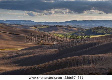 A beautifully lit valley with cultivated, plowed fields. Storm clouds over the valley