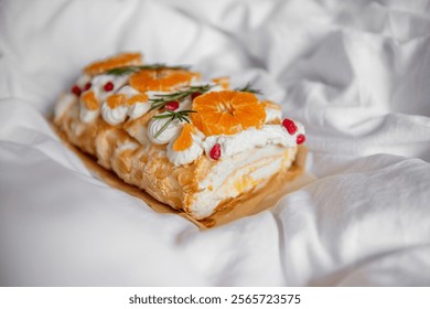 Beautifully presented dessert featuring orange slices, pomegranate seeds, cream, rosemary garnish on parchment, surrounded by soft white fabric for a cozy feel. Meringue Roll with Orange Curd dessert - Powered by Shutterstock