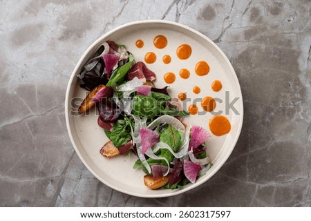 A beautifully presented salad showcases an array of fresh greens, colorful vegetables, and elegant sauces, perfect for an upscale European restaurant setting.
