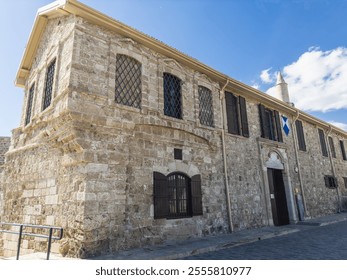 A beautifully preserved historic stone building in Larnaca showcasing traditional architecture, with arched windows, a wooden door, and cultural significance. - Powered by Shutterstock