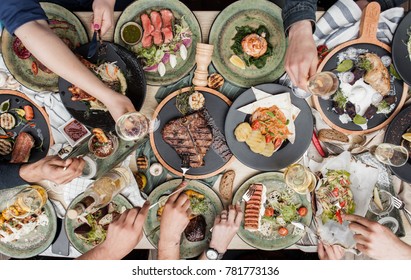 beautifully served table with different restaurant dishes and hands with glasses of wine