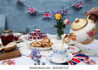 A beautifully staged VE Day 80th Anniversary celebration capturing the essence of British heritage and royal tradition. Set in a picturesque garden or village green, the vintage afternoon tea party 