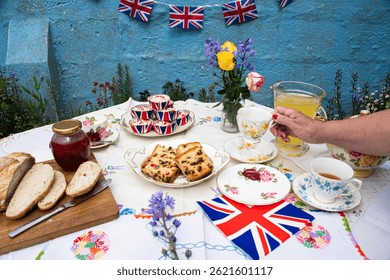 A beautifully staged VE Day 80th Anniversary celebration capturing the essence of British heritage and royal tradition. Set in a picturesque garden or village green, the vintage afternoon tea party 