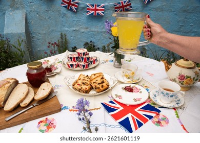 A beautifully staged VE Day 80th Anniversary celebration capturing the essence of British heritage and royal tradition. Set in a picturesque garden or village green, the vintage afternoon tea party 