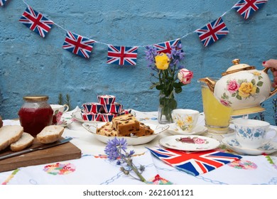 A beautifully staged VE Day 80th Anniversary celebration capturing the essence of British heritage and royal tradition. Set in a picturesque garden or village green, the vintage afternoon tea party 