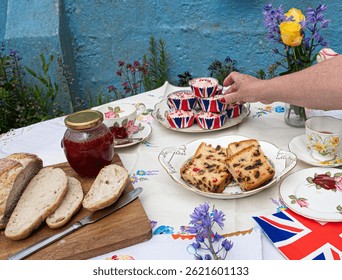 A beautifully staged VE Day 80th Anniversary celebration capturing the essence of British heritage and royal tradition. Set in a picturesque garden or village green, the vintage afternoon tea party 