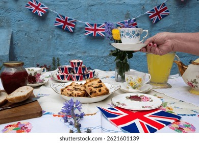 A beautifully staged VE Day 80th Anniversary celebration capturing the essence of British heritage and royal tradition. Set in a picturesque garden or village green, the vintage afternoon tea party 