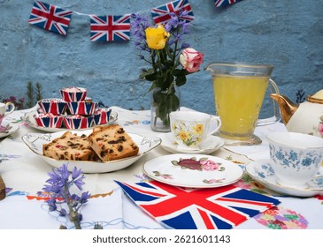 A beautifully staged VE Day 80th Anniversary celebration capturing the essence of British heritage and royal tradition. Set in a picturesque garden or village green, the vintage afternoon tea party 