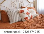 Beautifully styled bed features warm, rich toned bedding and charming decorative pillows with mushroom patterns against of metal forged headboard background. Bedding, home decor, interior design