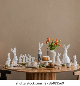 A beautifully styled Easter table setting with white ceramic rabbit figurines, a rustic cake, and fresh orange tulips in a textured vase. Warm neutrals and organic materials evoke a serene, festive atmosphere.