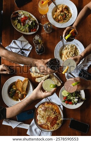 A beautifully styled flat lay of multiple Italian dishes on a rustic table, as hands toast with glasses. The elegant, moody ambiance captures the joy of sharing a gourmet meal in an Italian restaurant