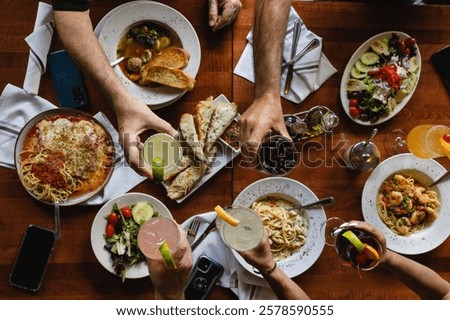 A beautifully styled flat lay of multiple Italian dishes on a rustic table, as hands toast with glasses. The elegant, moody ambiance captures the joy of sharing a gourmet meal in an Italian restaurant
